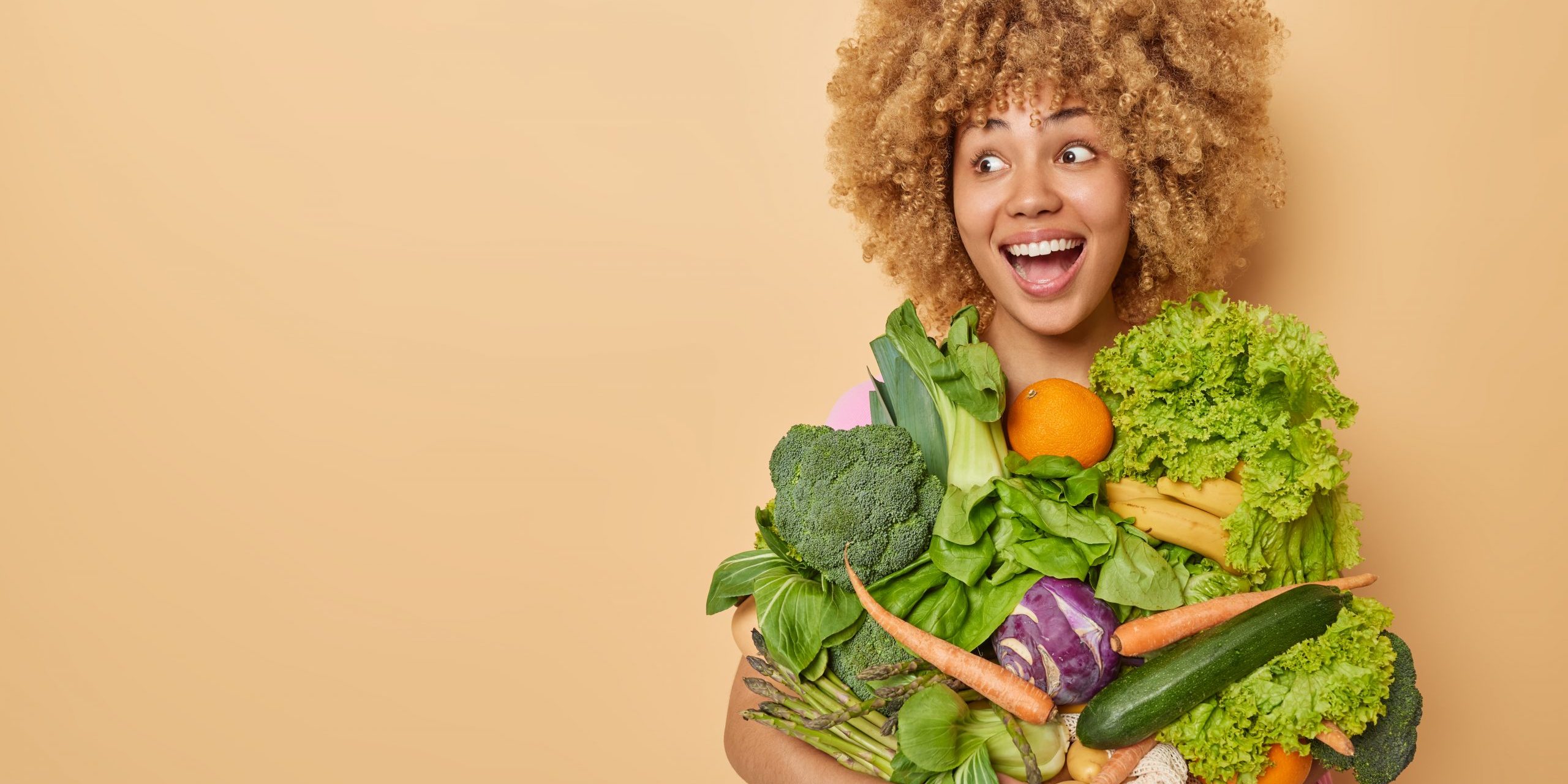 Horizontal shot of happy surprised woman reacts to something funny carries freshly picked vegetables from garden keeps to clean eating prefers vegetarian food poses indoor empty space for text